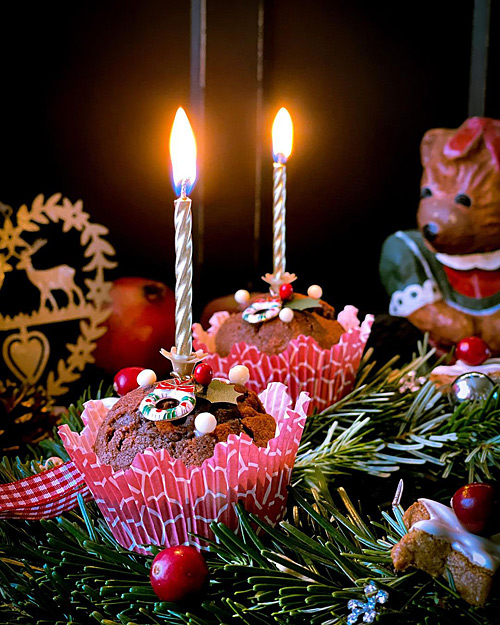 Frohe Weihnachten Adventskranz aus Tannenzweigen mit weihnachtlich verzierten Muffins Cupcakes mit brennenden Kerzen